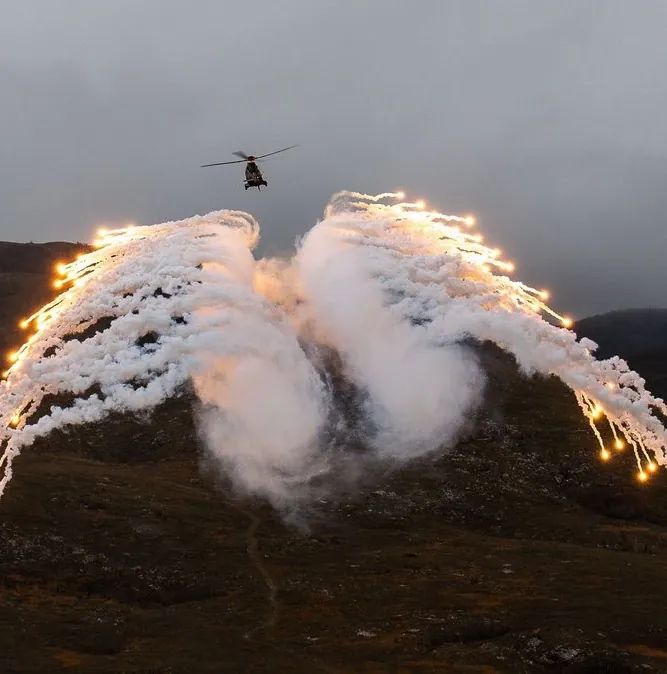 Helicopter deploying countermeasure flares over hills